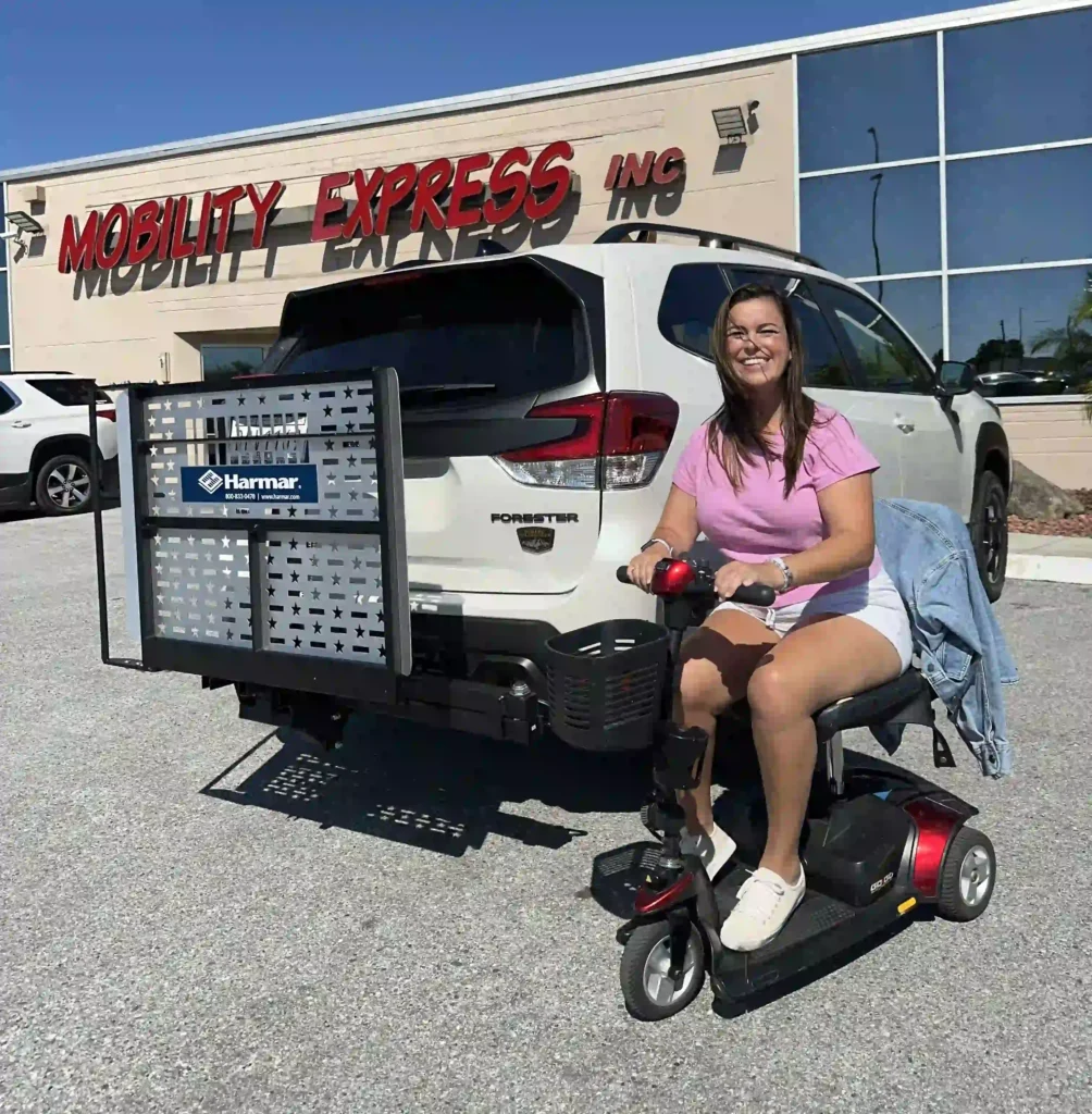 A woman in a pink shirt sits on a mobility scooter next to a white vehicle outside a store named "Mobility Express, Inc."