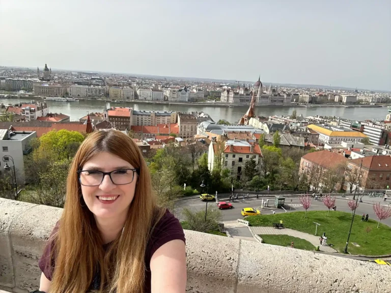 A panoramic view of Budapest featuring the Danube River, historic buildings, and lush greenery under a clear sky.