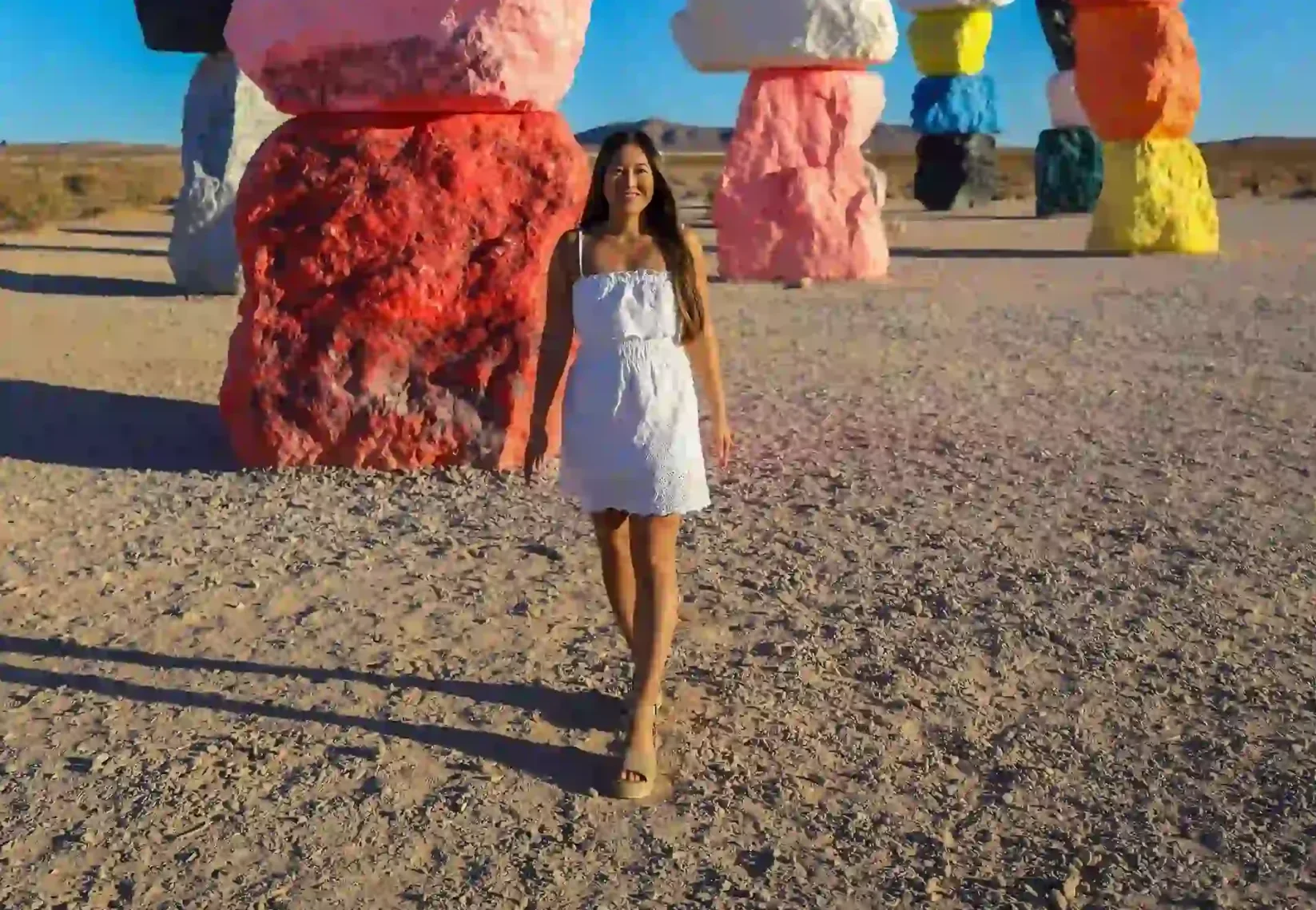 Woman in white dress walking amidst vibrantly colored stacked rocks in a desert landscape.