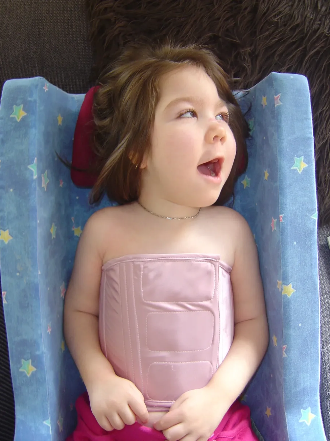 Toddler wearing a pink supportive bodice, lying in a blue star-patterned seat.