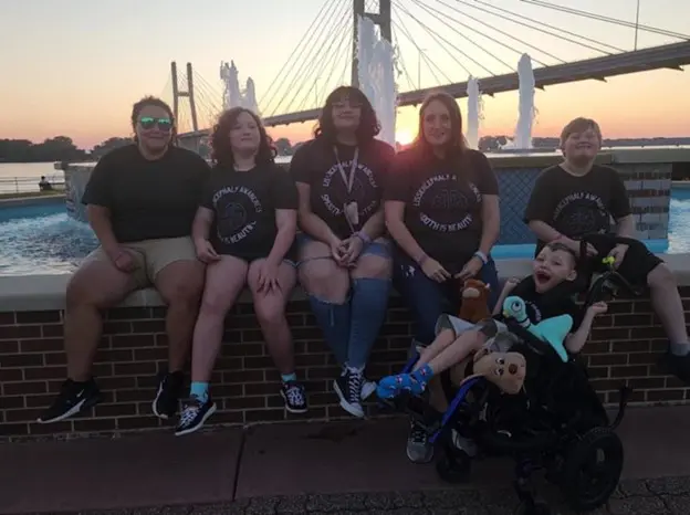 A group of six friends poses by a fountain at sunset, wearing matching black shirts, with a bridge in the background.