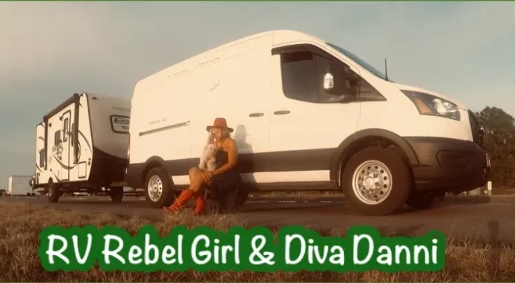 A woman sits on the ground beside a white RV, with a small dog, showcasing a nomadic lifestyle amid grassy surroundings.