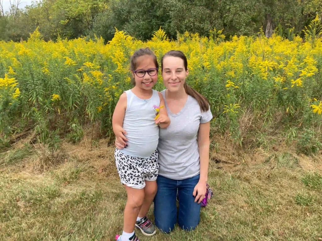 A woman and a young girl smile together in a field of vibrant yellow flowers, capturing a moment of joy and togetherness.