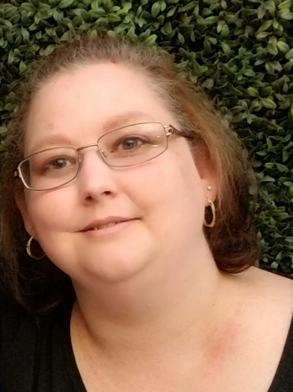 Woman with shoulder-length brown hair, wearing glasses and hoop earrings, smiling at the camera.