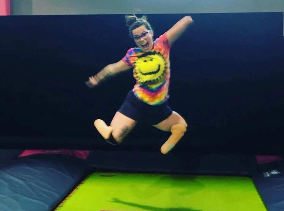 Person with prosthetic legs jumping in the air on a bright green trampoline.