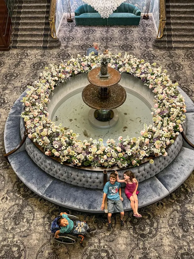 A circular fountain adorned with colorful flowers sits in a plush lounge area, featuring cozy seating and elegant decor.