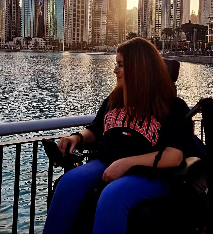 Woman in a wheelchair enjoying the sunset view of Dubai's skyline over a lake.