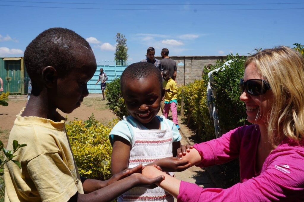 Children engage in a playful interaction outdoors, surrounded by greenery under a bright blue sky, showcasing friendship and joy.