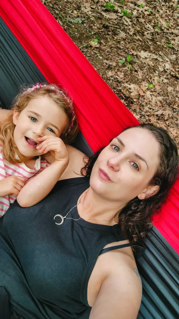 A woman and a young child lie together in a red and black hammock, both smiling at the camera.