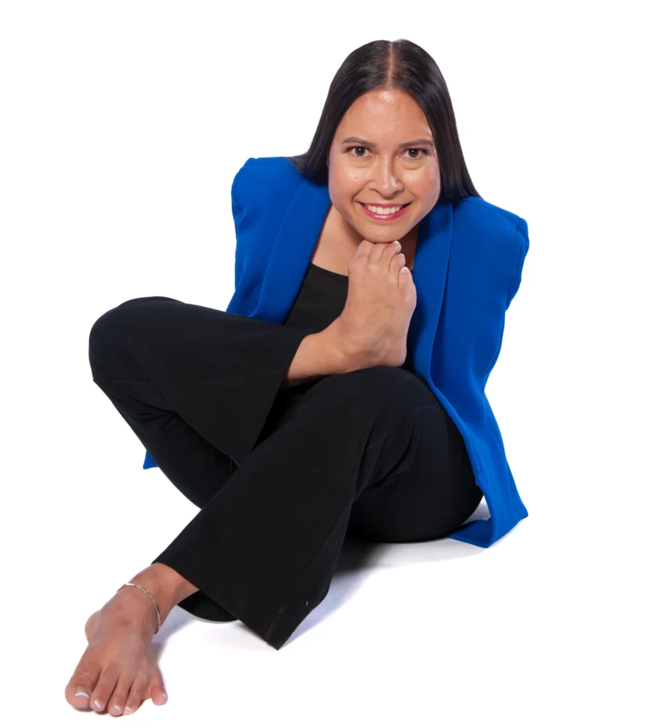 A professional portrait of Jessica Cox, a woman born without arms, sitting on the floor in a blue blazer and black pants, with one of her feet raised to her face.