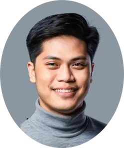 A headshot of a smiling man with black hair, wearing a gray turtleneck. The background is a solid gray.