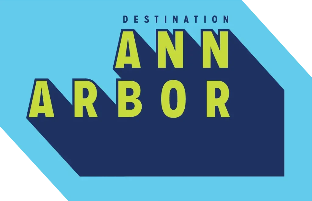 A graphic logo featuring the words "DESTINATION ANN ARBOR" in a stylized, blocky font. The text is lime green with deep navy blue drop shadows, set against a bright light-blue geometric background.