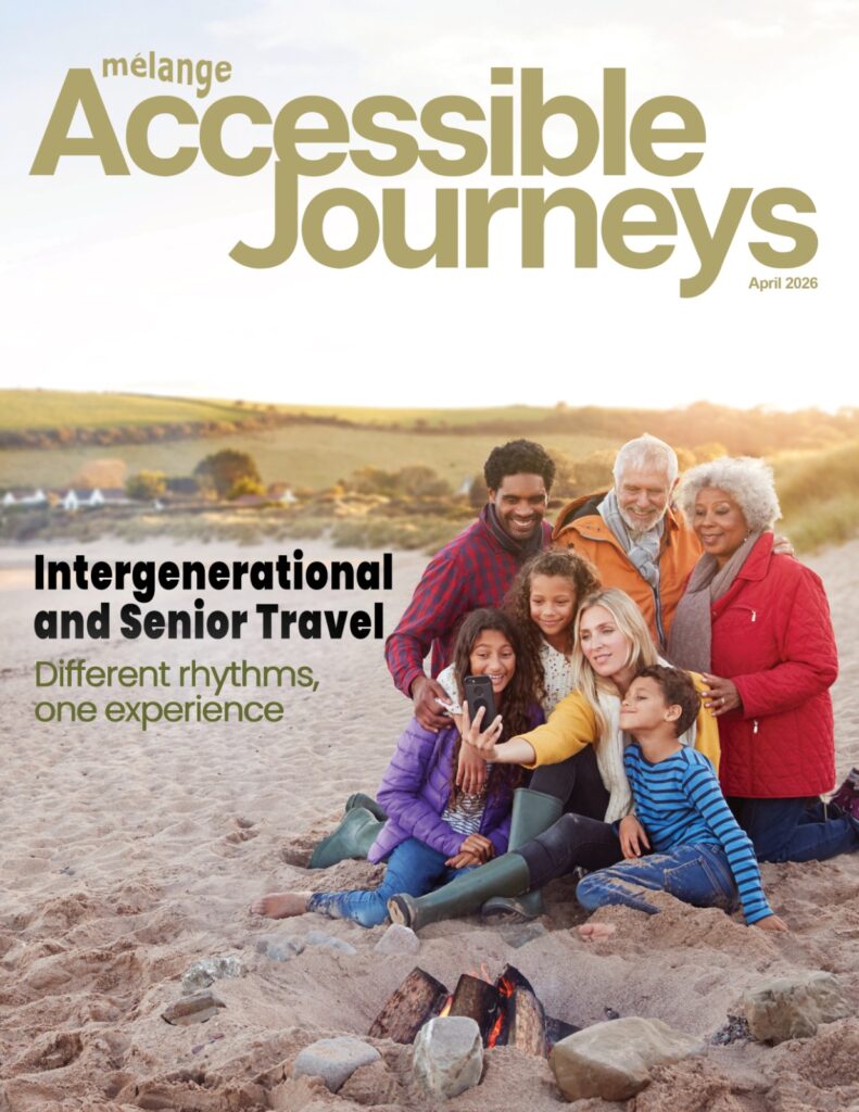 The cover of Mélange Accessible Journeys magazine (April 2026 issue) titled "Intergenerational and Senior Travel: Different rhythms, one experience." The image features a diverse, multi-generational family of seven—including grandparents, parents, and children—gathering closely on a sandy beach at sunset. A woman in the foreground holds a smartphone to take a group selfie while the family smiles, positioned near a small campfire built with stones and logs.