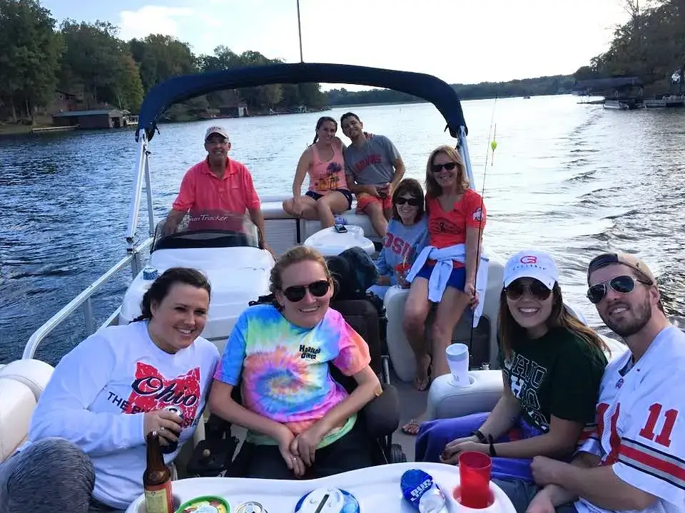 A large group of smiling friends and family posing together on a white pontoon boat at Cordry Lake, Indiana, with lush green trees and a calm lake in the background.