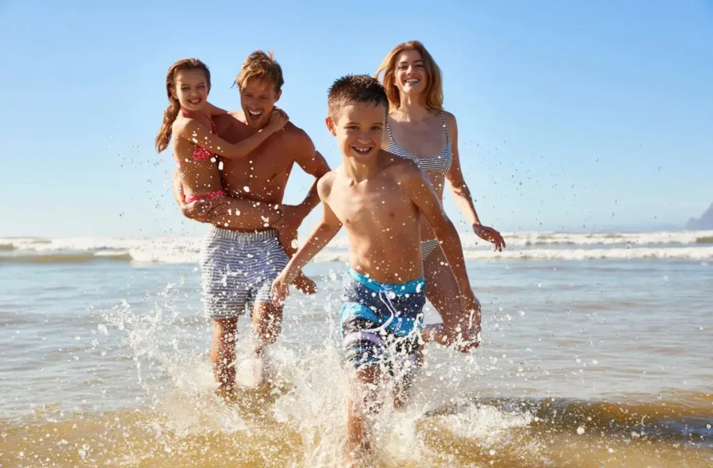 A happy family with two children splashing through ocean waves on a bright, sunny beach day.