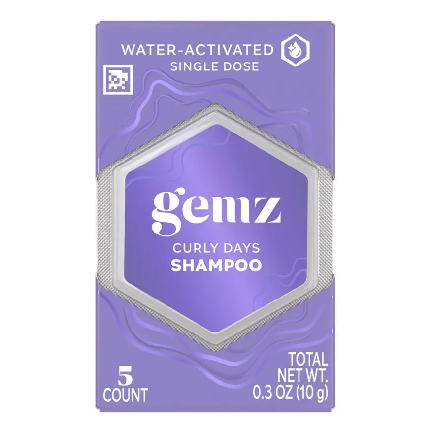 A lavender-colored package of Gemz Curly Days Shampoo, a water-activated single-dose hair care product. The packaging features a white hexagonal label with purple text and a QR-style NaviLens code in the top left corner for accessible product information.