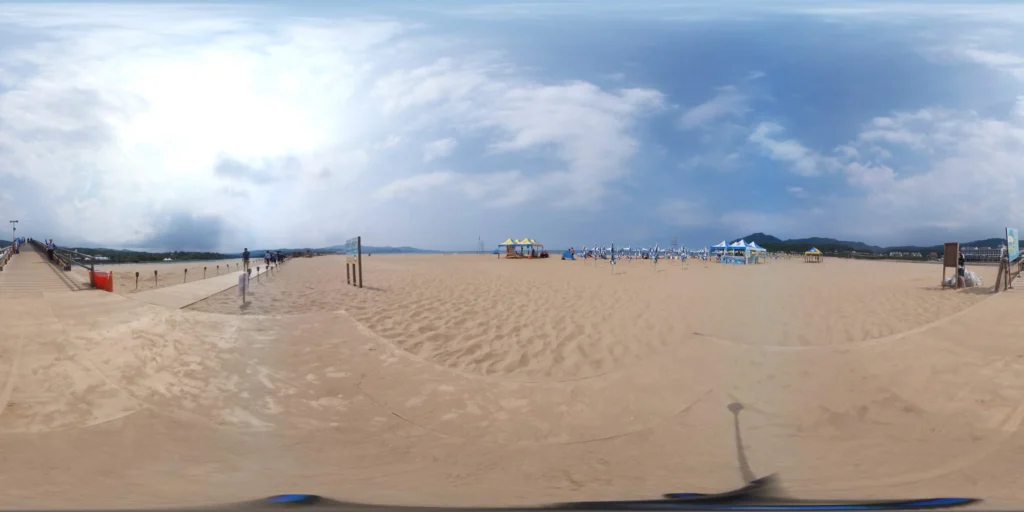 Wide panoramic view of Fulong Beach featuring golden sand, beach umbrellas, a wooden walkway, and blue skies with light clouds.