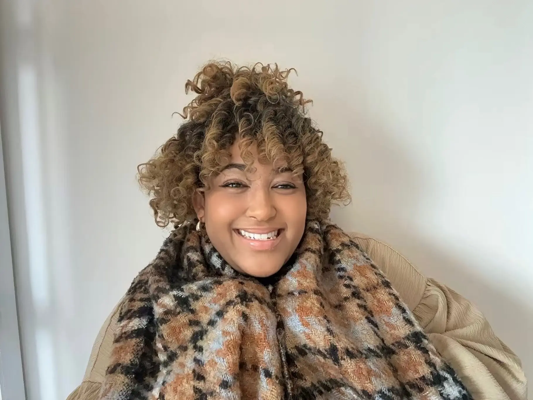 Portrait of a smiling woman with short curly curly hair wearing a cozy brown plaid scarf.