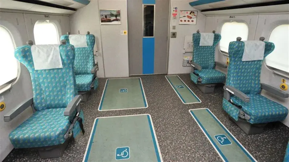 Interior view of an accessible High-Speed Rail train car with teal patterned seats and designated wheelchair parking spaces on the floor.