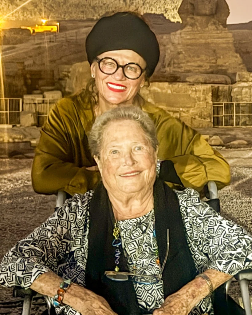 Two smiling women posing together at night with the Great Sphinx of Giza illuminated in the background during an evening tour in Egypt.