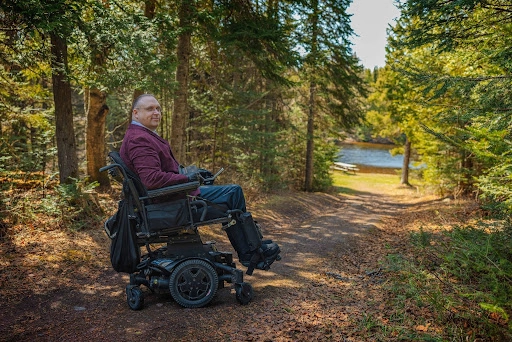 A man using a motorized wheelchair pauses along a dirt forest trail near a river in Thunder Bay.