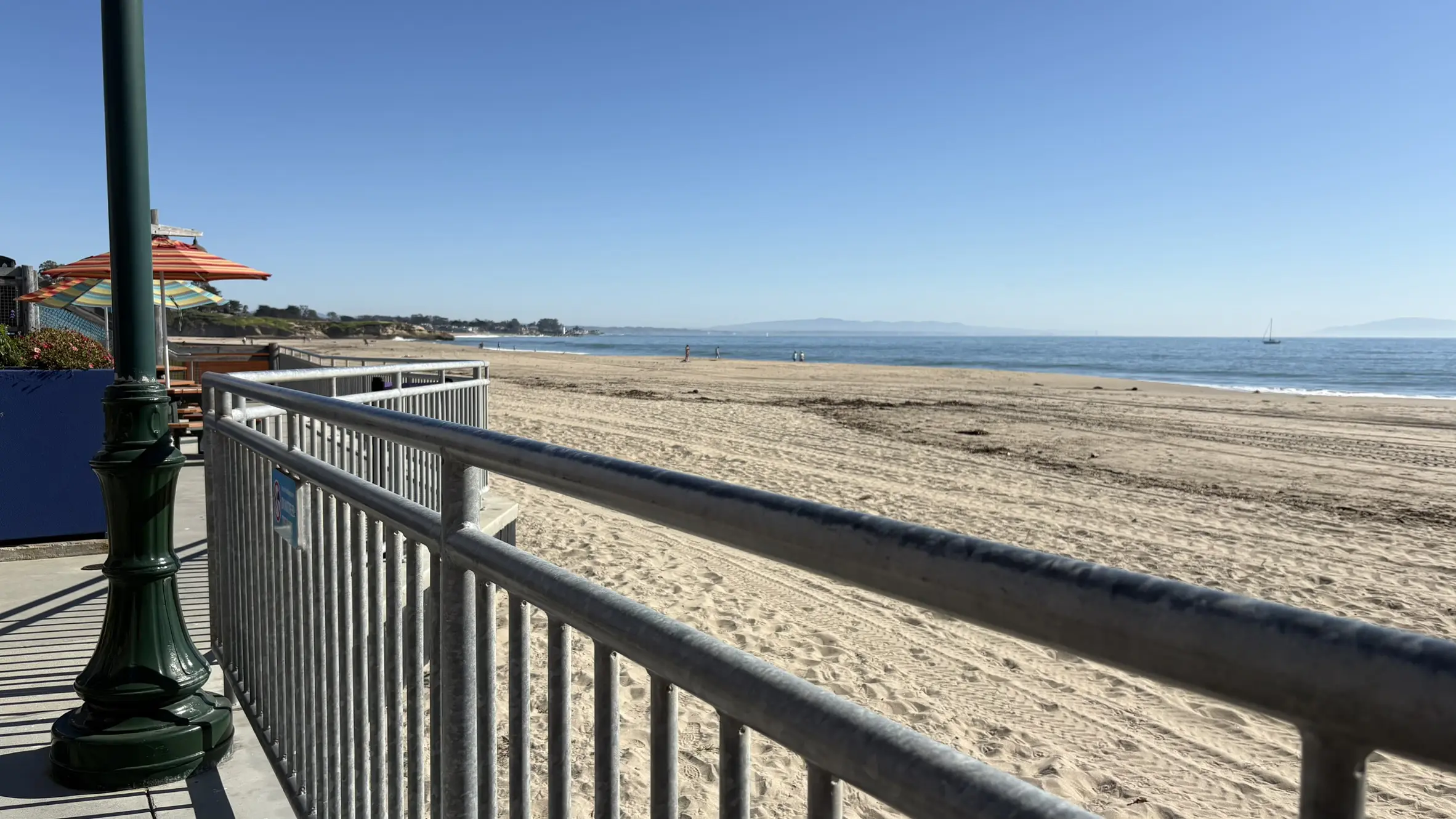 View from a boardwalk railing looking out over a wide, sandy beach and calm ocean waters in Santa Cruz, California.