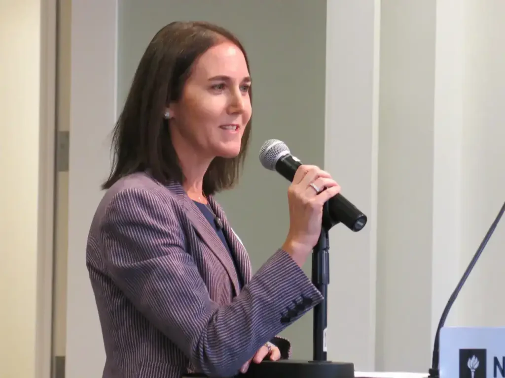 Hearing loss advocate Shari Eberts speaking into a microphone at a presentation event.