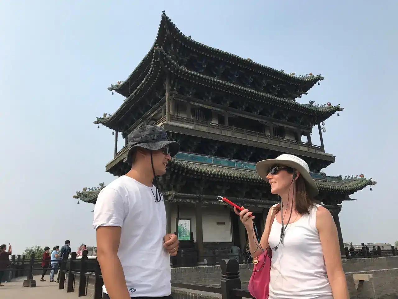 hari Eberts using an assistive listening device while talking to a companion during a trip in front of a historic pagoda.