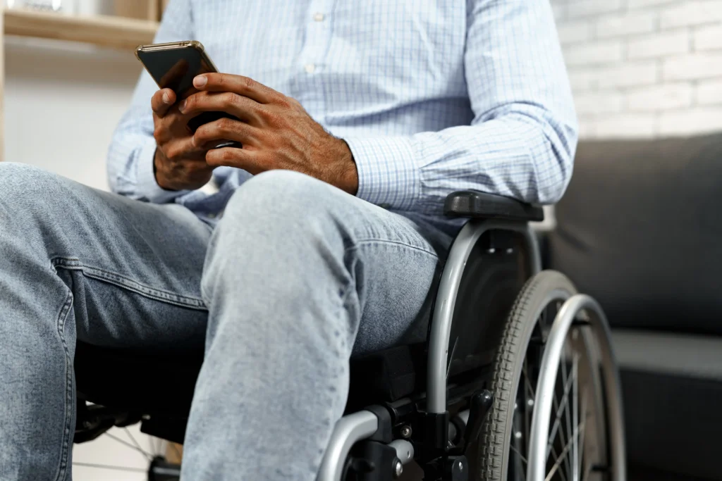 Close-up of a man sitting in a wheelchair using a smartphone in a modern home setting.