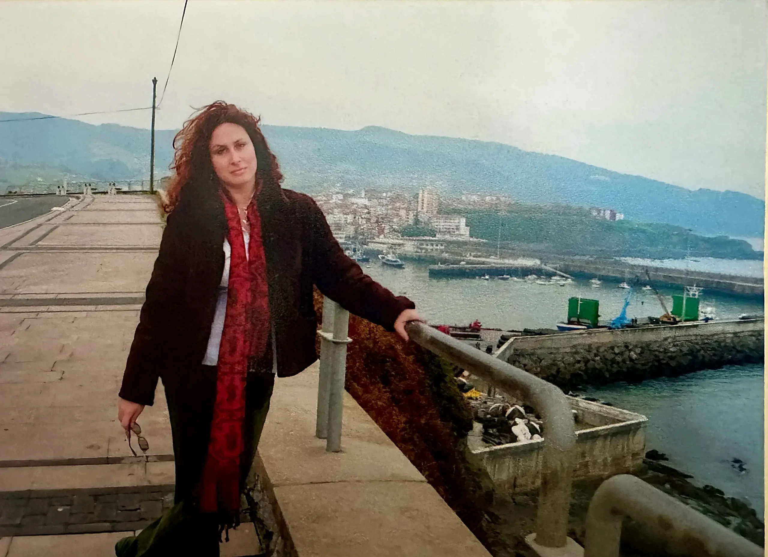 Woman leaning against a railing overlooking the harbor and coastal town of Bermeo, Spain.