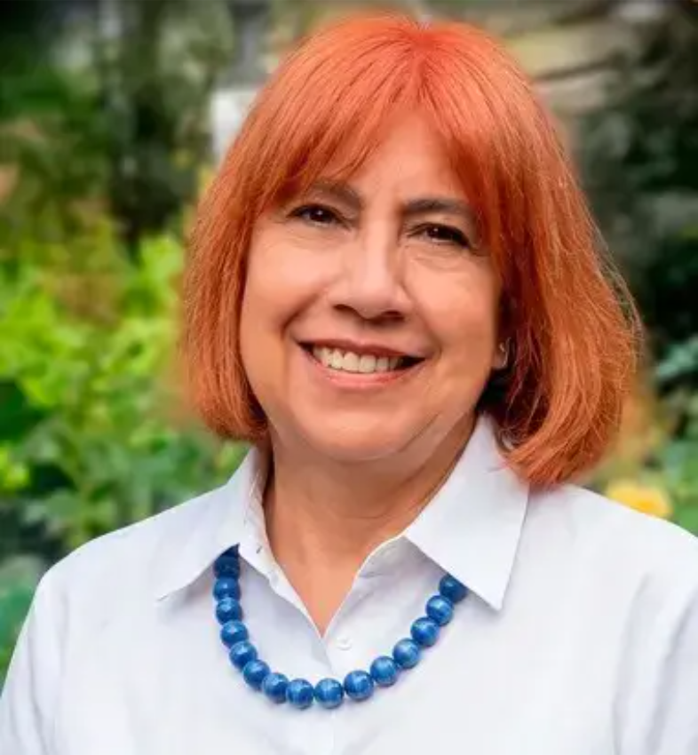 Portrait of a smiling woman with reddish-orange hair wearing a white collared shirt and a blue beaded necklace.